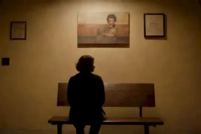 Joven de ascendencia latina sentado pensativo en un banco de una oscura sala de cine